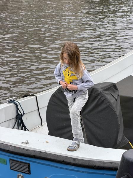 A young child wearing a Pikachu shirt stands on a blue and white boat, looking down at something on the deck